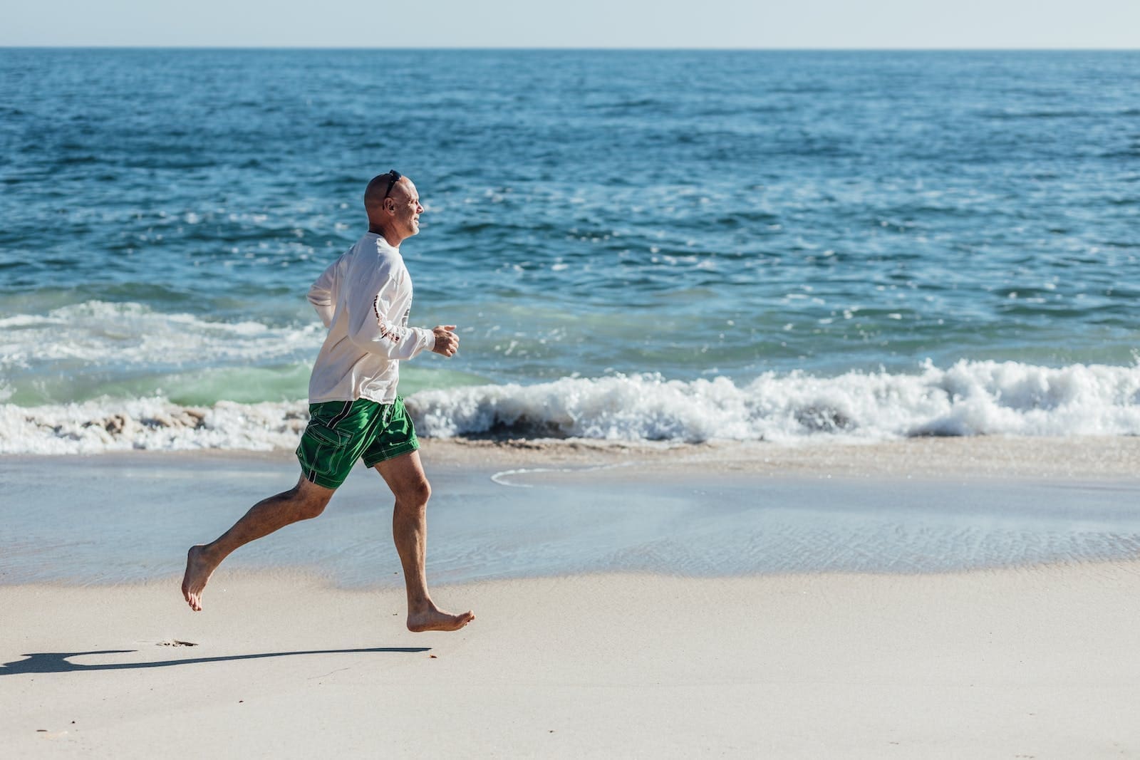 Man in White Shirt and Green Shorts Running on Beach